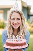 A blonde woman wearing a party hat and holding a birthday cake