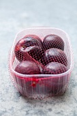 Several plums in a plastic pot wrapped in netting