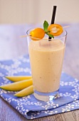An exotic smoothie with mango and kumquats on a blue napkin on a wooden tabletop