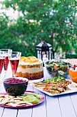 A table in the garden, laid with prawn skewers, beetroot dip, spinach salad and a trifle