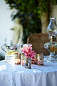 Gedeckter Tisch mit Öllampe, Windlichtern, Blumen und Limonadenkrug