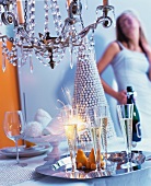 Champagne flutes & sparklers on tray below chandelier with party guest in background