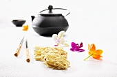 Egg noodles, chopsticks, a teapot and orchid flowers