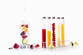 A glass of water with fruits in, and frozen fruits and juices in glass tubes