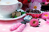 Cappuccinotasse neben Dessertbesteck und Kaffeebohnen in Papiermanschetten auf dekoriertem Gartentisch