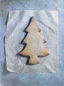 A Christmas tree biscuit dusted with icing sugar, on a piece of grease-proof paper