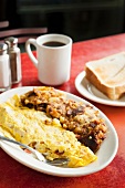 Bacon and Tomato Omelet Served with Hash on a White Plate; Coffee and Toast on a Diner Table