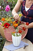 Frau arrangiert Sommerblumen in einer Vase auf Gartentisch