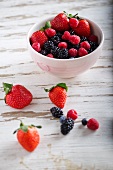 Assorted berries in a bowl and on a wooden surface