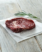 Raw beef steak with salt and rosemary on baking paper