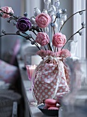 Arrangement of artificial flowers in fabric-wrapped vase on window sill