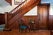 Baroque chair next to modern side table in front of half-height wood panelling on wall of wooden staircase in traditional hallway