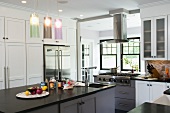 Free-standing kitchen island below modern pendant lamps with coloured glass shades in white country-house kitchen