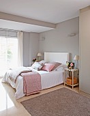 Double bed with blankets and scatter cushions in pastel grey and pink in bedroom with grey walls
