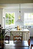 Weiß lackierte Landhausküche mit Küchenblock im Vintagelook; Essplatz aus Naturholz im Vordergrund
