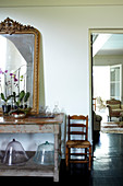 Orchids and gilt-framed mirror on old wooden table next to doorway with view into living room with traditional upholstered armchairs