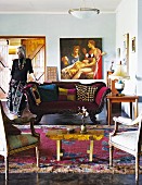 Interior in eclectic mixture of styles with antique seating and collection of unusual objet; woman leaning on sofa