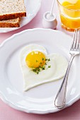 A heart-shaped fried egg with cress, toast and orange juice
