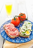 An Open Ham, Egg, Cucumber and Avocado Sandwich on a Blue and White Plate; Tomatoes
