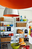 Orangefarbene Industrieleuchten und Metallregale in einfacher Küche mit bunten Küchenutensilien