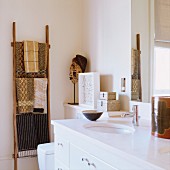 Modern, white bathroon vanity next to a ladder towel rack and patterned hand towels