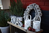 Christmas arrangement on terrace: lanterns, decorative letters, wreath of pine cones, small potted conifers