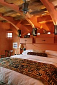 Schlafzimmer unter dem Dach - Doppelbett an lachsfarbener Wand mit Schränkchen auf Ablage in gleicher Farbe und Blick in sichtbaren Dachstuhl aus Holz