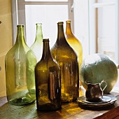 Old, empty bottles lit from behind, silver jug and ceramic sphere on cabinet