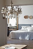 Blick durch offenen Durchgang auf französisches Bett und Bistrotisch vor altem Spiegel; Kristalllüster im Vordergrund