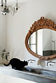Katze im Becken eines Beton Waschtischs mit antikem Spiegel und minimalistisch originellen Wandarmaturen