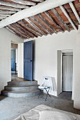 Betonstufen vor blauer Holztür und rustikale, offene Dachuntersicht in puristischem Schlafraum