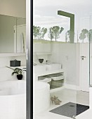 Blick durch Glaswände in weisses Bad mit runder Wanne; Spiegelung der umgebenden Natur auf Glaselement