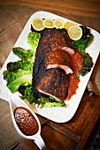 Barbecued Pork Ribs on a Platter with Lemon and Lettuce; Extra Sauce on the Side