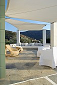 Zwischen Mauerstützen gespannte Sonnensegel auf mediterraner Terrasse mit bequemen Sitzgelegenheiten