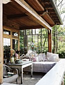 Cozy corner of a country home veranda with day bed and pillows in front of a stained glass wall and a view of trees