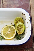 Lemon slices, squeezed limes and rosemary in a roasting tin