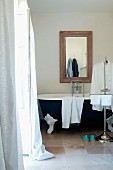 Towels and man's shirts on valet stand in front of vintage clawfoot bathtub below framed mirror on wall in modern interior