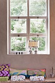 Cushions on bench below window with square casements and pair of postmodern table lamps on sill