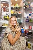 Junge Frau isst Joghurt vor dem Kühlschrank