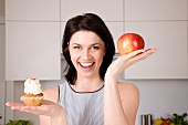 A woman holding up an apple and a cupcake