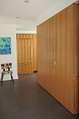 Wooden fitted cupboard in modern hallway with view into open-plan kitchen with matching wooden fronts
