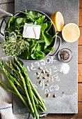 A still life of spinach, asparagus, cress, feta, pine nuts, lemons, salt and pepper