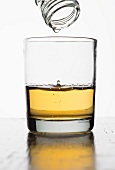 The last drop of whiskey dripping out of a bottle into a glass