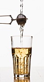 Hot water being poured into a glass through filled tea-brewing tongs