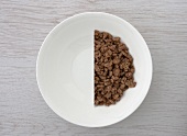 A halved portion of chocolate crisped rice in a white bowl (view from above)