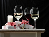 Rot- und Weißwein in Gläsern, daneben Geschenke