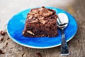 A chocolate brownie on a blue plate with a spoon