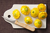 Several yellow patty pan squash on a chopping board with a knife