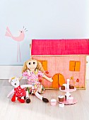 Stoffpuppen mit bunten Kleidern vor einem Puppenhaus