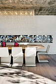 Designer Essplatz mit Freischwingerstühlen an langer Tafel und Spiegelstreifen an der Rückwand; dekoratives Beleuchtungselement an roher Betondecke